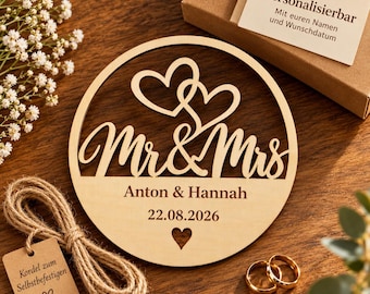 Può includere: Una targa circolare in legno chiaro con la scritta Mr & Mrs tagliata al laser, due cuori intrecciati, i nomi incisi Anton & Hannah e la data 22.08.2026. Include un piccolo cuore intagliato, dello spago di juta e una scatola regalo.