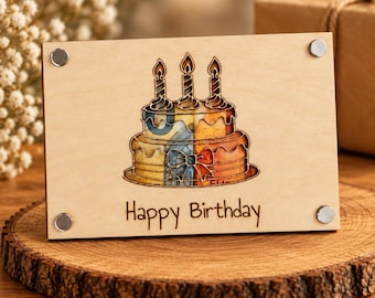 Può includere: Una targa rettangolare in legno chiaro con una torta di compleanno a due piani incisa al laser e tre candele accese. Il design della torta è riempito con un motivo a banconote colorate. Il testo Happy Birthday è inciso sotto la torta.