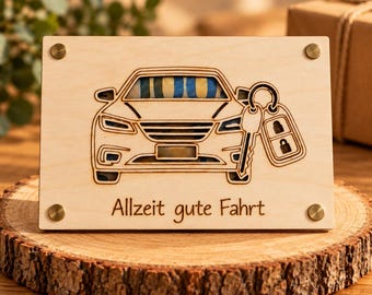 Può includere: Una targa rettangolare in legno chiaro con un'incisione laser della vista frontale di un'auto e di una chiave. Il testo "Allzeit gute Fahrt" è inciso sotto l'auto. Quattro piccoli rivetti in metallo color ottone fissano gli angoli.