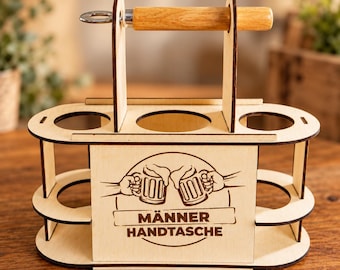 Può includere: Un portabottiglie da birra in legno chiaro con manico centrale e apribottiglie in metallo. Il pannello frontale presenta un'incisione laser di due boccali di birra che brindano e il testo MÄNNER HANDTASCHE.