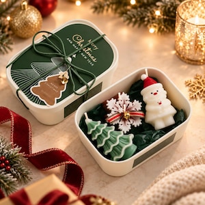 Peut inclure: Une boîte cadeau rectangulaire blanche avec un couvercle vert foncé portant l'inscription Merry Christmas and Happy New Year, nouée avec une ficelle verte et une étiquette en forme de sapin. Trois bougies en forme de bonhomme de neige, flocon et sapin.