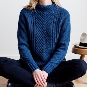 May include: A deep blue long-sleeve sweater featuring a high mock neck and a prominent vertical chevron cable knit pattern down the center. The garment has ribbed cuffs and a textured knit construction, paired with solid black trousers.