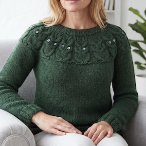 May include: A dark forest green long-sleeve knit sweater featuring a round neckline and a textured yoke pattern. The yoke is decorated with a series of raised cable-knit owl motifs, each accented with small, dark circular buttons for eyes.