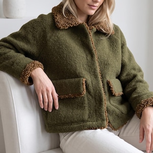 Puede incluir: Una chaqueta texturizada de color verde oliva con cuello de sherpa marrón, puños de sherpa marrón y dos bolsillos delanteros con ribete de sherpa marrón. La chaqueta tiene un cierre frontal de botones y un acabado exterior grueso y afelpado.