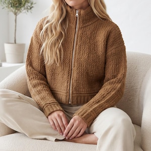 Peut inclure: Une veste zippée marron à la texture polaire, dotée d'un col montant et d'une fermeture éclair en métal argenté. Le vêtement présente des manches longues avec des poignets côtelés et un ourlet côtelé assorti, dans une matière douce et duveteuse.