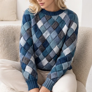 May include: A long-sleeve knit sweater featuring a woven basket-weave pattern in various shades of blue, gray, and white. The garment has a round neckline and ribbed cuffs at the wrists and waist, constructed with a textured, multi-colored yarn design.