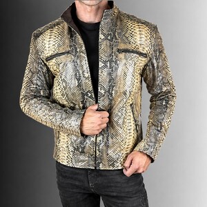 Puede incluir: Una chaqueta con estampado de piel de serpiente en tonos beige, marrón claro y negro. La prenda tiene cuello alzado, cremallera frontal completa y dos bolsillos horizontales con cremallera en el pecho. El forro interior es de color marrón oscuro.