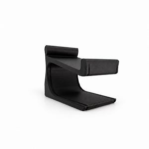 Peut inclure: Un support de casque noir mat présentant un profil incurvé en forme de C avec une base plate et un repose-tête conçu pour maintenir un casque. La structure est solide et de couleur uniforme, avec des bords lisses et un design continu et épuré.