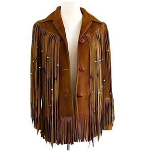 May include: A brown suede jacket featuring long fringe detailing across the chest and sleeves. The jacket includes three dark brown buttons down the front, a classic collar, and small white beads attached to several of the fringe strands.
