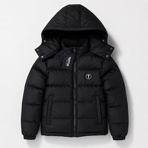 Op de afbeelding: Een zwart gewatteerd jack met een capuchon, een ritssluiting over de hele lengte en elastische boorden. Het jack heeft een rond logopatch op de linkerborst met een pijl omhoog en een zwart TRAPSTAR-merklabel aan de ritssluiting bevestigd.