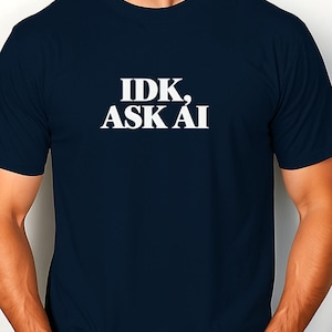 Könnte beinhalten: Ein dunkelblaues T-Shirt mit kurzen Ärmeln und Rundhalsausschnitt, das den weißen Schriftzug "IDK, ASK AI" in einer fetten Serifenschrift mittig auf der Brust trägt. Das Kleidungsstück hat eine Standardpassform mit einem schlichten Design.