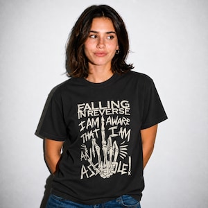Może przedstawiać: Czarny t-shirt z krótkim rękawem z grafiką przedstawiającą szkieletową dłoń wykonującą gest środkowego palca. Tekst brzmi: FALLING IN REVERSE I AM AWARE THAT I AM AN ASSHOLE! Wzór jest nadrukowany w postarzanym, złamanych odcieniu bieli.