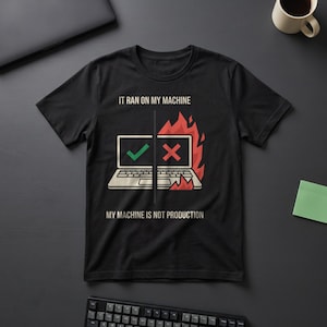 May include: A black short-sleeved t-shirt featuring a graphic of a laptop split in half. The left side shows a green checkmark, and the right side shows a red X with flames. Text reads: IT RAN ON MY MACHINE and MY MACHINE IS NOT PRODUCTION.
