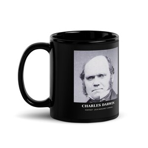 May include: A black ceramic mug featuring a black and white photographic portrait of Charles Darwin. Below the portrait, the text reads CHARLES DARWIN and PORTRAIT - JULIA MARGARET CAMERON. The mug has a curved handle and a glossy finish.