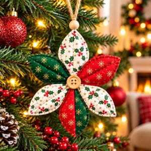 May include: A fabric star-shaped Christmas ornament featuring six quilted petals in alternating patterns of red, green, and cream with holly and snowflake prints. A small wooden button is centred in the middle, and a jute twine loop is attached.