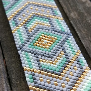 Peut inclure: Un bracelet en perles avec un motif géométrique dans des tons de blanc, gris, vert et or.