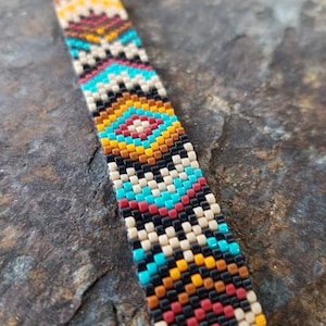 May include: A colorful beaded bracelet with a geometric pattern in shades of red, orange, yellow, black, white, and turquoise.