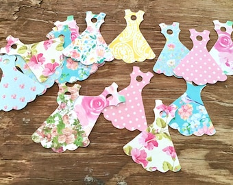 May include: Assortment of paper dress cutouts with various floral and patterned designs in pink, blue, and yellow. The cutouts are perfect for crafting, scrapbooking, or party decorations.