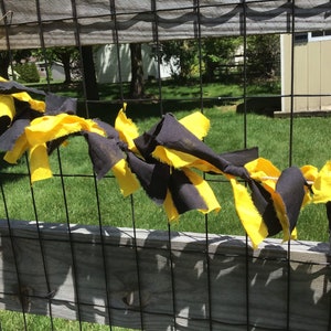 May include: A black and yellow fabric garland strung across a wooden fence. The garland is made of strips of fabric tied together.