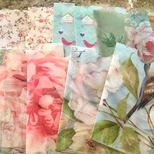 May include: A collection of decorative paper envelopes with floral and bird designs. The envelopes feature various patterns, including pink roses, small pink flowers, and birds with birdhouses. The envelopes are arranged on a wooden surface.
