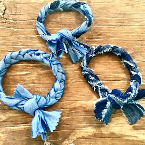 May include: Three braided denim rope dog toys in blue and dark blue. The toys are tied in a knot at the end.