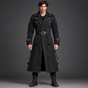 Op de afbeelding: Een lange zwarte trenchcoat met een gestructureerde kraag, meerdere klepzakken op de borst en heupen, schouderkleppen en een bijpassende riem met een zilveren gesp. De jas is voorzien van metalen D-ringen en verstelbare bandjes op de mouwen.
