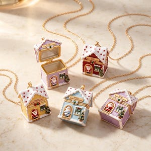 May include: Five miniature house-shaped pendants on gold-tone chains. Each pendant features a hinged roof, a Santa Claus figure in the doorway, a small Christmas tree, and text reading Santa's North Pole Workshop. Colours include lavender, red, yellow, and blue.