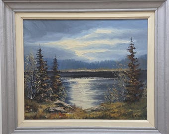 May include: An oil painting in a gray and cream frame depicting a landscape with a dark lake, tall evergreen trees, and a cloudy sky. The water reflects a bright light source from the horizon, while the foreground features rocky terrain.