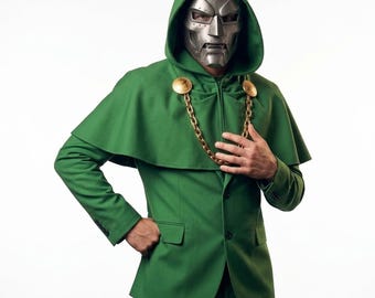 Puede incluir: Una chaqueta verde con capucha y una capa a juego sujeta a los hombros por una cadena de color dorado. La prenda incluye una máscara facial de color plateado metálico con un diseño mecánico detallado que cubre la cara y la cabeza.