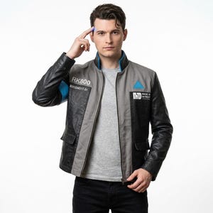 Könnte beinhalten: Eine graue und schwarze Jacke mit blauem Kragenfutter und einer blauen Armbinde am rechten Ärmel. Auf der Brust befinden sich der Text RK800, eine Seriennummer, ein blaues Dreiecksemblem und der Text MADE IN DETROIT mit Logo über der Tasche.