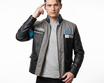 Puede incluir: Una chaqueta gris y negra con forro de cuello azul y un brazalete azul en la manga derecha. El pecho presenta el texto RK800, un número de serie, un emblema de triángulo azul y el texto MADE IN DETROIT con un logotipo sobre el bolsillo.