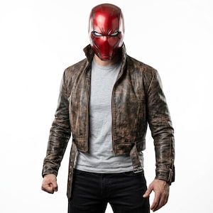 May include: A metallic red full-face helmet with white eye slits paired with a distressed brown leather jacket featuring a belted waist, worn over a plain light grey t-shirt and dark trousers. The jacket has long sleeves and a high collar.