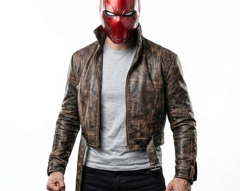 Puede incluir: Un casco integral de color rojo metálico con ranuras blancas para los ojos, combinado con una chaqueta de cuero marrón desgastado con cinturón en la cintura, sobre una camiseta gris claro lisa y pantalones oscuros.