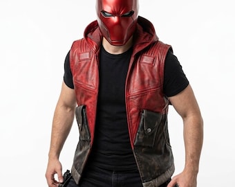 Puede incluir: Un casco integral de color rojo metálico con ranuras oscuras para los ojos, combinado con un chaleco sin mangas con capucha. El chaleco presenta un diseño bicolor con una parte superior roja desgastada y una inferior marrón, con dos bolsillos.