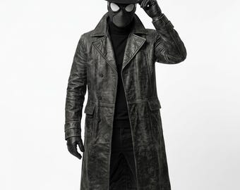 Puede incluir: Una gabardina larga de cuero gris carbón desgastado con frente de doble botonadura, solapas anchas y dos bolsillos grandes con solapa. El conjunto incluye un sombrero fedora negro, un suéter de cuello alto negro, pantalones negros y guantes de cuero negro.