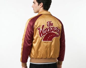 Puede incluir: Una chaqueta bomber de satén dorada y granate con cuello, puños acanalados y cintura. La parte posterior muestra un parche bordado con el texto The Wanderers en letra cursiva, acentuado por un gráfico de carretera estilizado en granate y blanco.