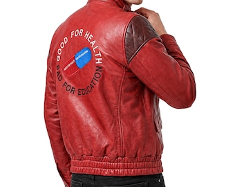 Puede incluir: Una chaqueta de cuero roja con cuello alzado, paneles acolchados en los hombros y dobladillo acanalado. La espalda muestra un gráfico bordado de una píldora roja y azul con el texto circular "GOOD FOR HEALTH BAD FOR EDUCATION" en blanco.