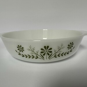 May include: A white milk glass round baking dish with integrated side handles. The exterior features a repeating pattern of dark olive green flowers and delicate leafy sprigs encircling the bowl, creating a simple and clean aesthetic.