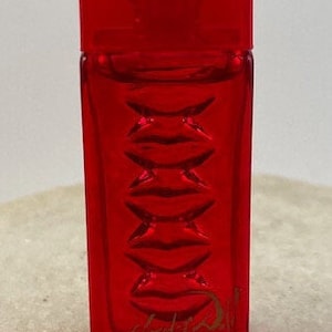 Può includere: Un flacone di profumo in vetro rosso con un'etichetta dorata che dice "Juicy Couture" e "Viva La Juicy" in un font corsivo.