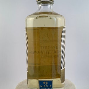 May include: A clear glass bottle with a gold cap and a blue and white label that reads "Mibelle Buchs/AG 150 ml. 3.20".