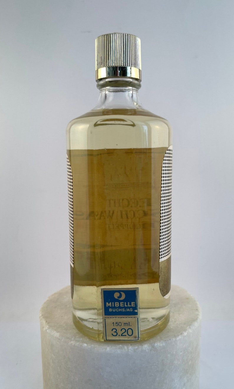 May include: A clear glass bottle with a gold cap and a blue and white label that reads "Mibelle Buchs/AG 150 ml. 3.20".