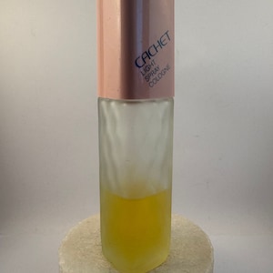 Può includere: Un flacone di Colonia Cachet Light Spray in vetro rosa e trasparente.