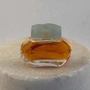 May include: A small, clear glass bottle of perfume with a light green cap. The bottle is filled with a golden liquid.