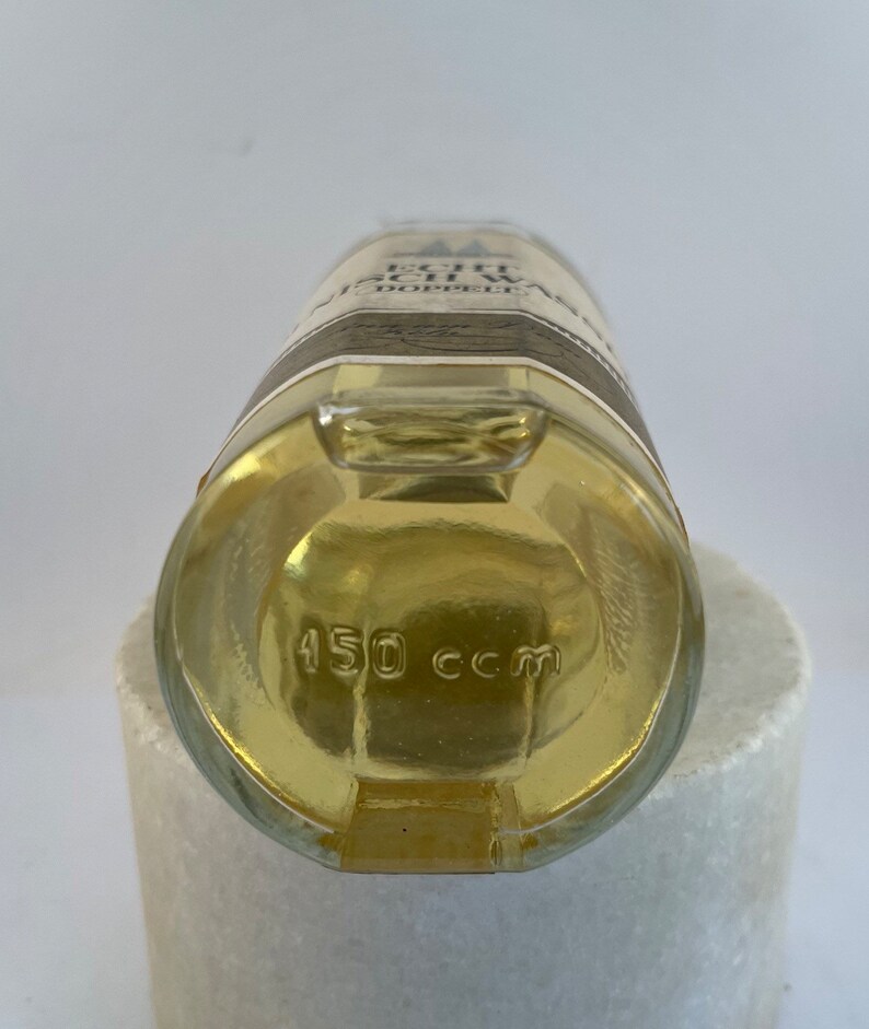 May include: A clear glass bottle with a yellow liquid inside. The bottle has a label with the text "Echt Schwarzw&auml;lder Kirschwasser" and "Doppelfeine" on it. The bottom of the bottle has the text "450 ccm".