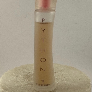 Peut inclure: Un petit flacon de parfum transparent avec le mot "PYTHON" imprimé verticalement en marron. Le flacon a une forme incurvée et un bouchon teinté de rouge. La marque "Trussardi" est imprimée en bas.