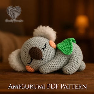 May include: A light gray crocheted koala amigurumi with a dark brown nose, peach-colored cheeks, and fluffy white ear tufts. A bright green leaf is attached to its back. The text Crochet Paradise and AMIGURUMI PDF PATTERN are visible.