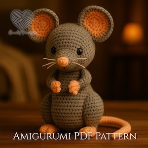Peut inclure: Une souris amigurumi crochetée grise avec l'intérieur des oreilles, le nez, les mains, les pieds et la queue de couleur pêche. La souris a des yeux en perles noires et des moustaches en fil blanc. Le texte Crochet Paradise et AMIGURUMI PDF PATTERN est visible.