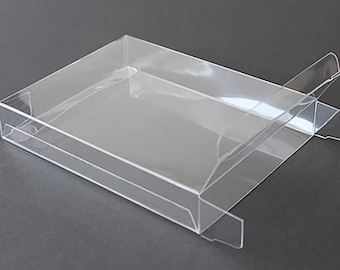 May include: A rectangular, clear plastic box with a shallow base and a hinged lid. The container is transparent, allowing for full visibility of the interior space. It features a simple folding design with integrated tabs for secure closure.