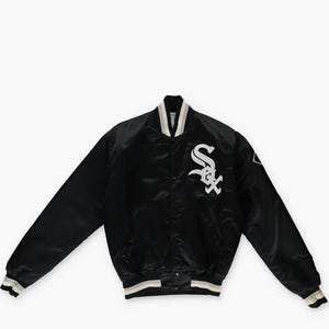 Może przedstawiać: Czarna satynowa kurtka typu varsity z białym haftowanym logo Chicago White Sox na lewej piersi. Kurtka posiada zapięcie na zatrzaski, długie rękawy oraz prążkowane ściągacze przy mankietach i kołnierzu z biało-szarymi paskami.