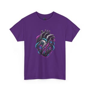 Puede incluir: Una camiseta morada de manga corta con un gráfico central de un corazón mecánico. El corazón está representado en tonos gris oscuro y negro con placas de circuito integradas, cables brillantes en azul cian y rosa magenta, y placas metálicas.